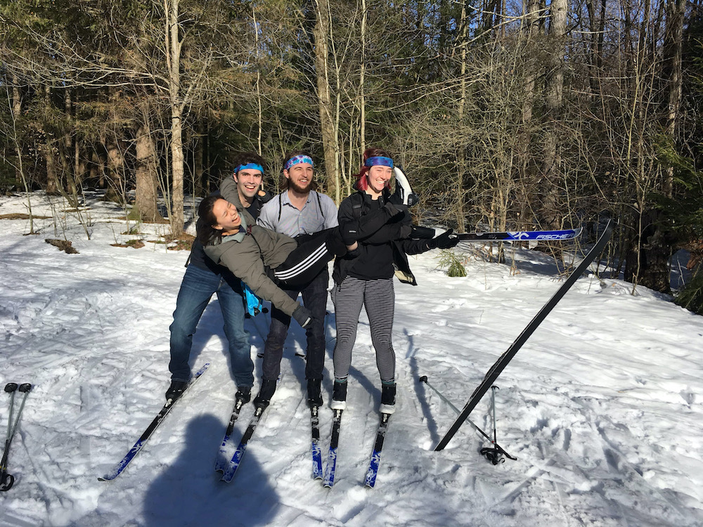 Three math people wearing cross country skis holding a fourth math person who has lost one of her skis.